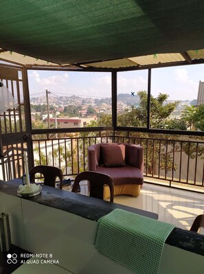 Ein Balkon mit einer Couch und Sesseln, einem Tisch mit einer Kerze und Blick auf eine Stadtlandschaft.