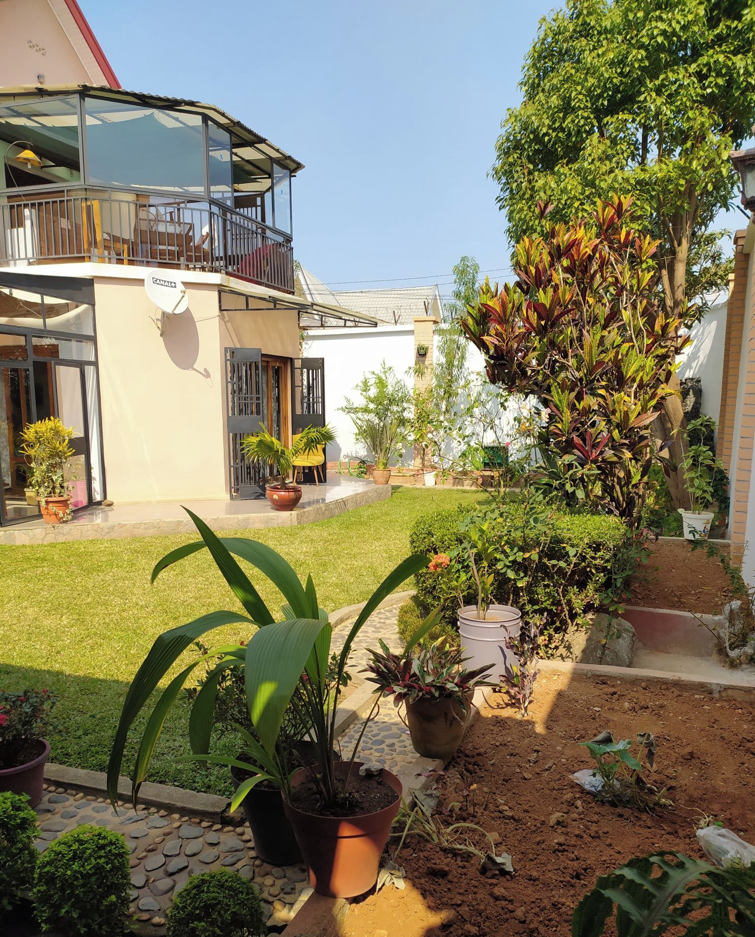 A house with a balcony, potted plants, and a garden area.