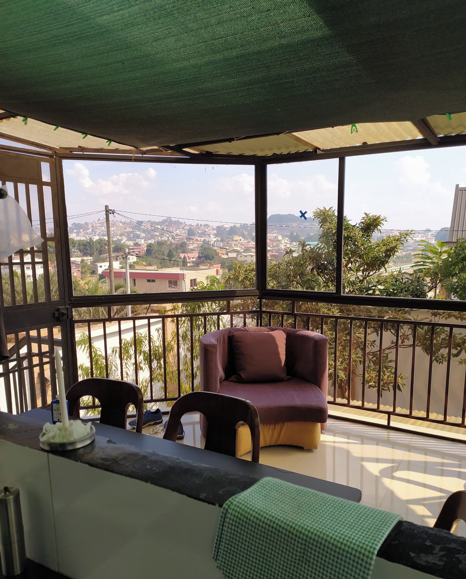 A balcony with a sofa and chairs, a table with a candle, and a view of a cityscape.