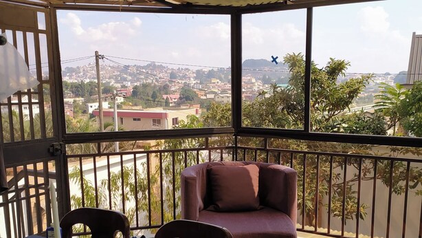 A balcony with a sofa and chairs, a table with a candle, and a view of a cityscape. -  Grace Guesthouse (Antananarivo)