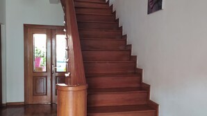 A wooden staircase with a handrail, leading to a door with a view of greenery outside. -  Grace Guesthouse (Antananarivo)