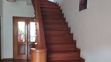 A wooden staircase with a handrail, leading to a door with a view of greenery outside.