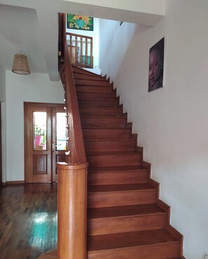 A wooden staircase with a handrail, leading to a door with a view of greenery outside. -  Grace Guesthouse (Antananarivo)