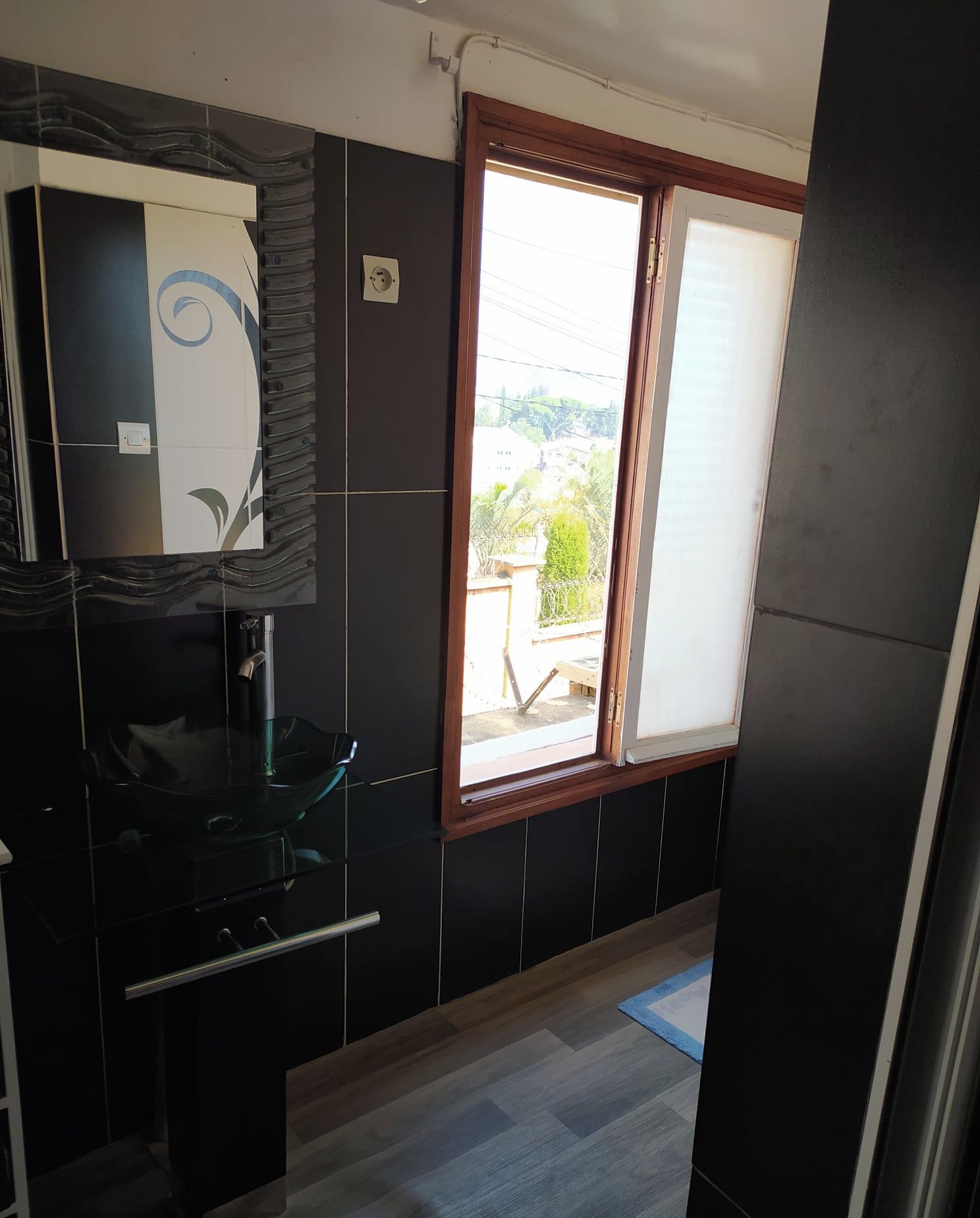 A bathroom with a glass sink, a mirror, and a window with a view of the outside.
