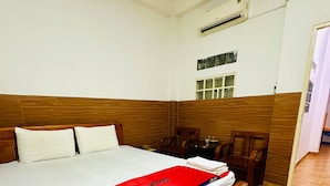 A single-bed room with a wooden headboard, a red blanket, a wooden nightstand, and a chair.
