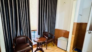 A room with a wooden floor, two wooden chairs, a small round table, and a white cabinet.