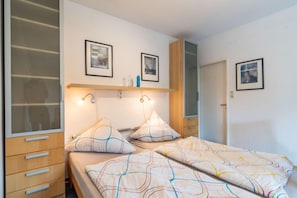 A bedroom with two beds, a wardrobe, and a mirror.