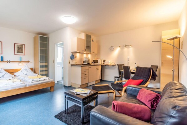 A compact living space with a bed, a sofa, a dining area, and a kitchenette.