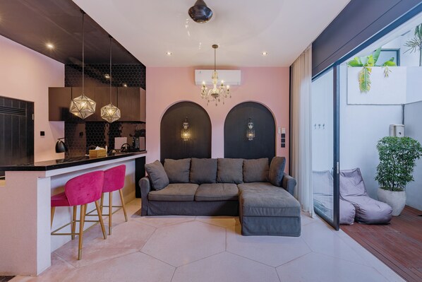 A modern living space with a kitchen area, a sofa, and a bar with two pink chairs. - Liminal Palace Villa 3 by Betterplace (Canggu)