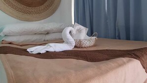 A neatly made bed with a brown blanket, a large woven headboard, and a basket of white towels. - Fomo hostel palawan (Puerto Princesa)