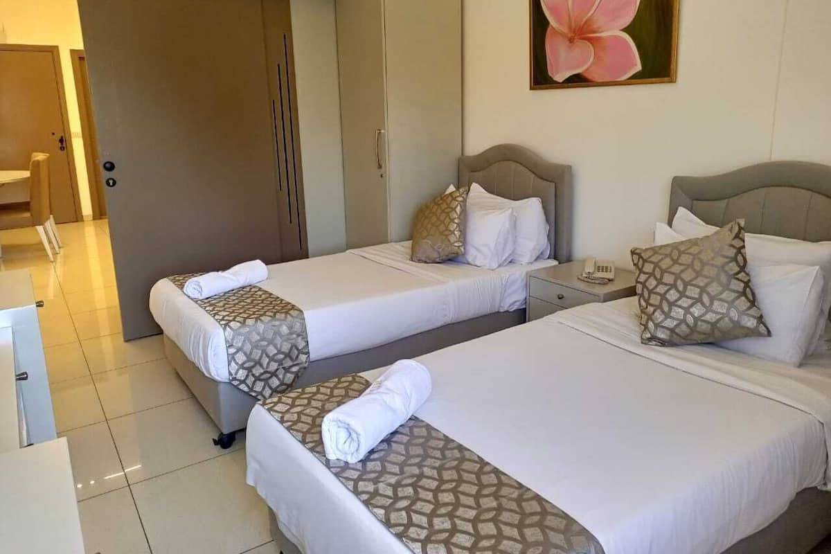 A hotel room with two beds, a wardrobe, a desk, and a painting on the wall.