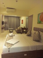 A hotel room with a large bed, a desk, a sofa, and a TV.