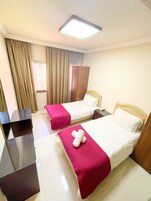 A hotel room with two beds, a desk, a wardrobe, and a window with curtains.