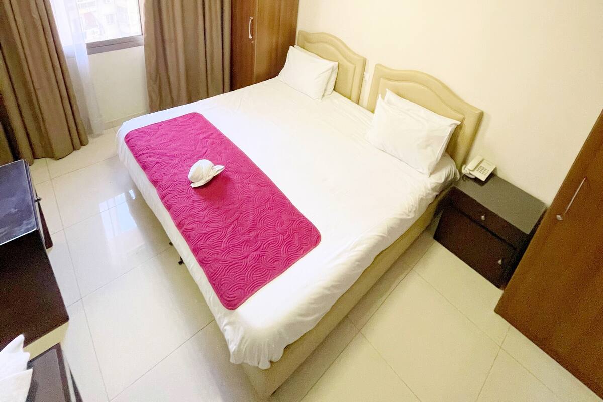 A hotel room with a bed, a desk, a wardrobe, and a window with curtains.