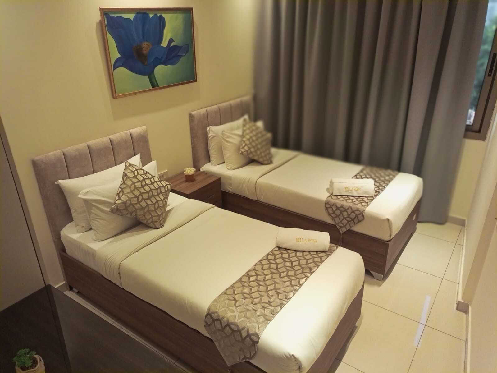 Habitación de hotel con dos camas, cada una con cabecera, almohadas y una colcha de estampado geométrico. Hay un cuadro en la pared y una ventana con cortinas.