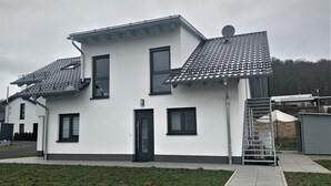 Une maison moderne à deux étages, avec un toit en tuiles, une porte d’entrée et un petit porche.