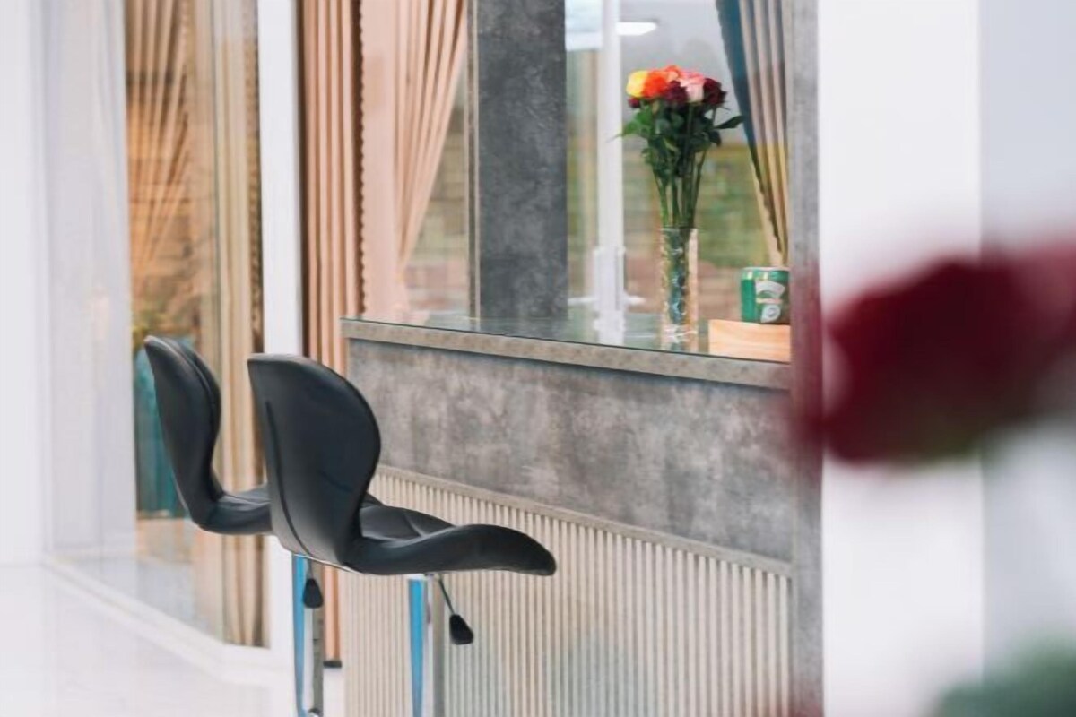A modern room with a large window, a chair, and a vase with flowers on the windowsill.