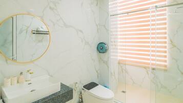 A bathroom with a marble wall, a round mirror, a sink, a toilet, and a shower with blinds.