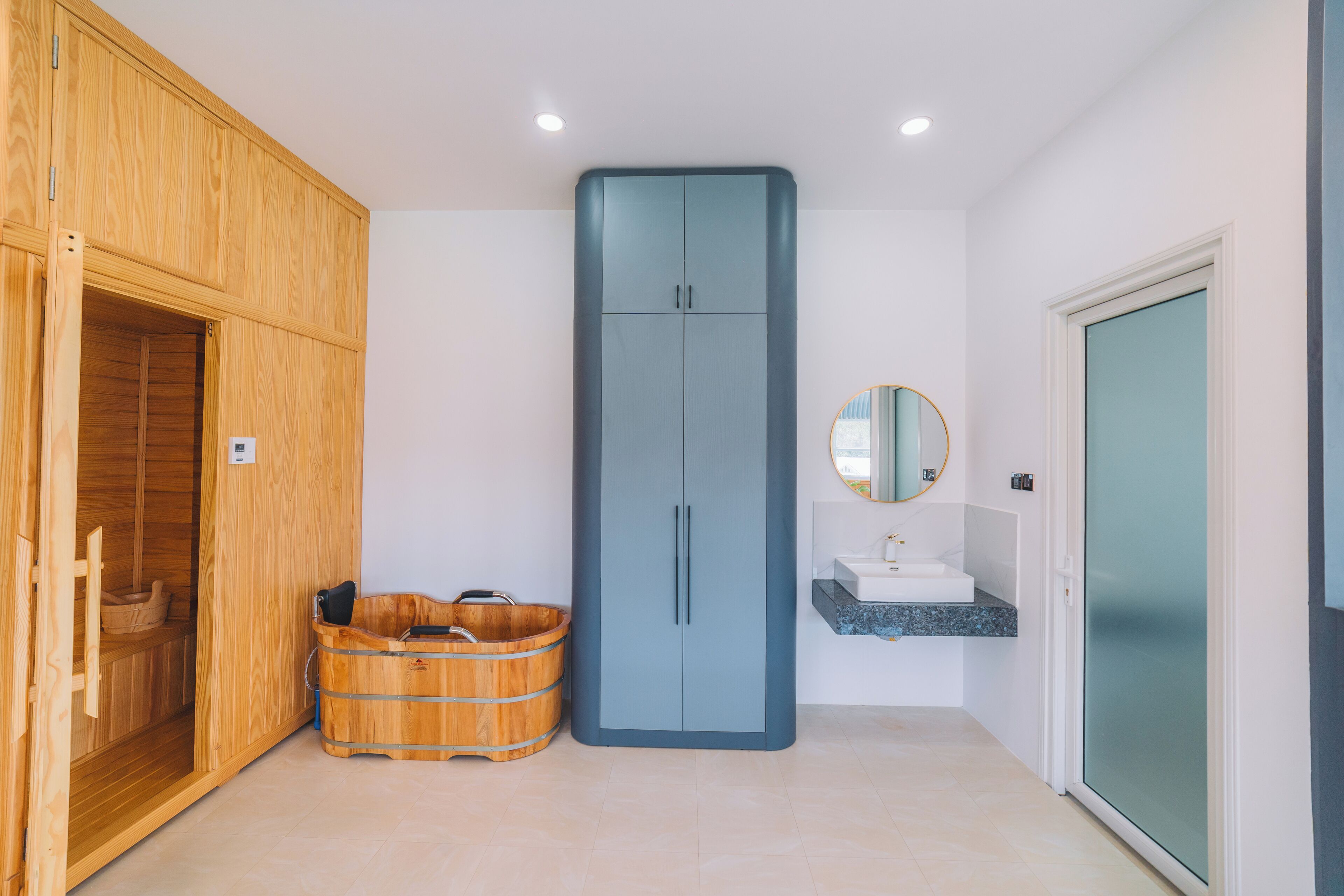 A modern bathroom with a wooden sauna, a tall blue cabinet, and a sink with a mirror.
