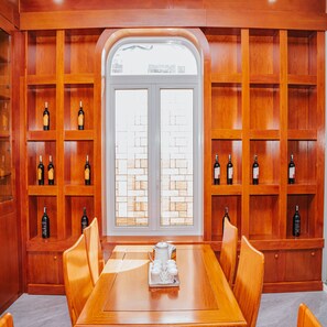 A dining area with a wooden table and chairs, surrounded by wooden shelves with wine bottles. - Quy Tai Premium Hotel (Xuan Huong - Da Lat)
