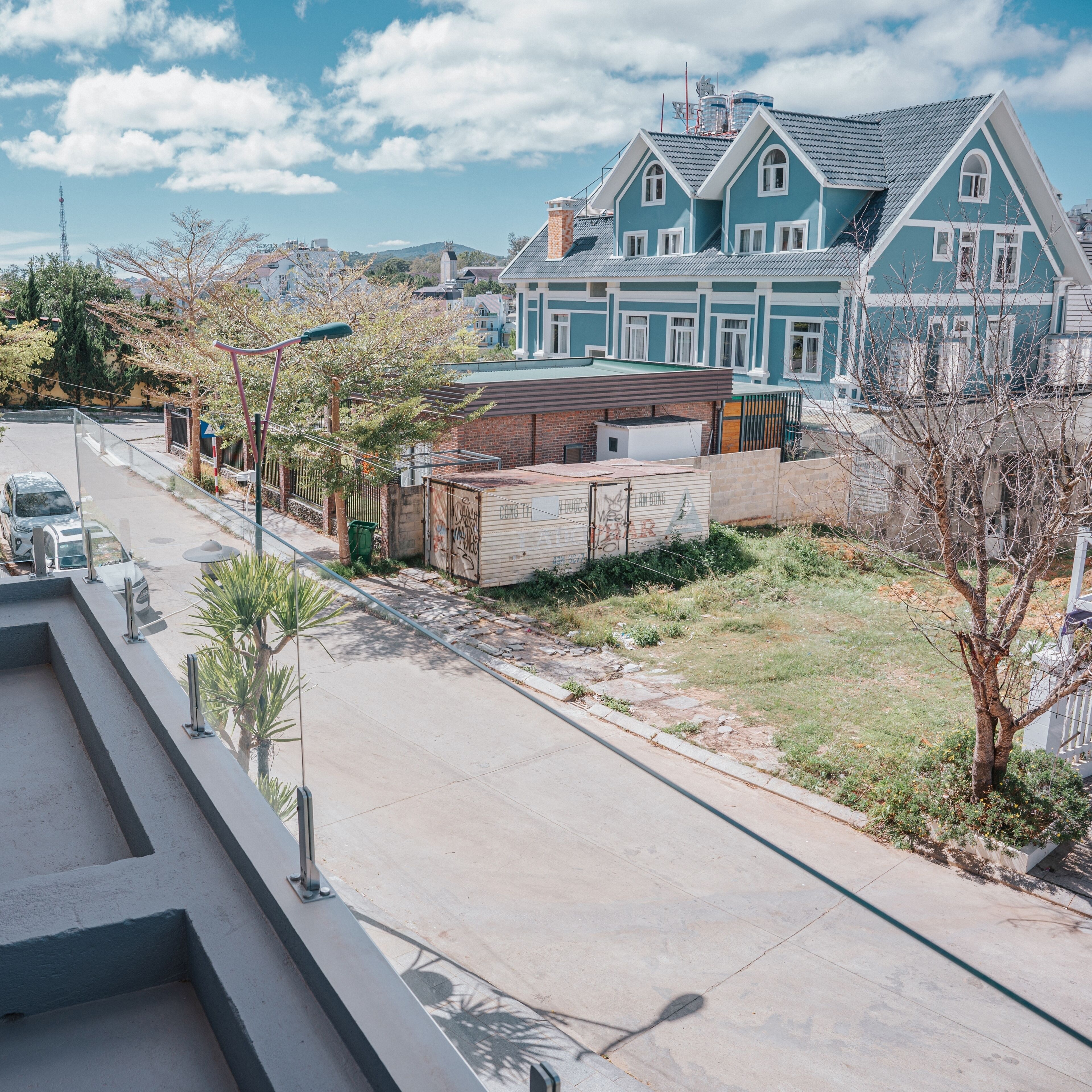 Un barrio residencial con una casa grande azul, una calle pavimentada y un pequeño patio cercado.