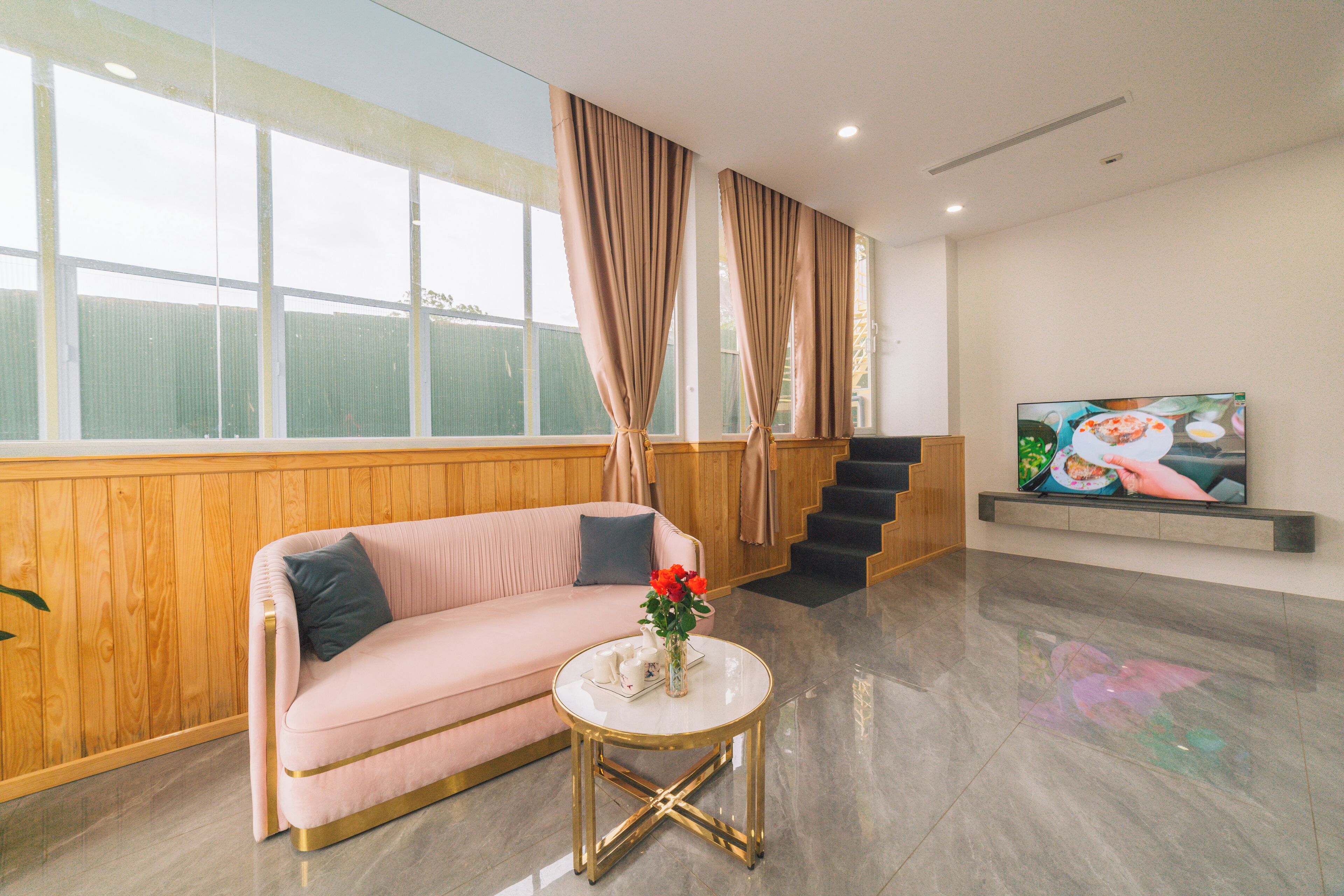 A modern living room with a pink sofa, a round coffee table, and a large window with curtains.