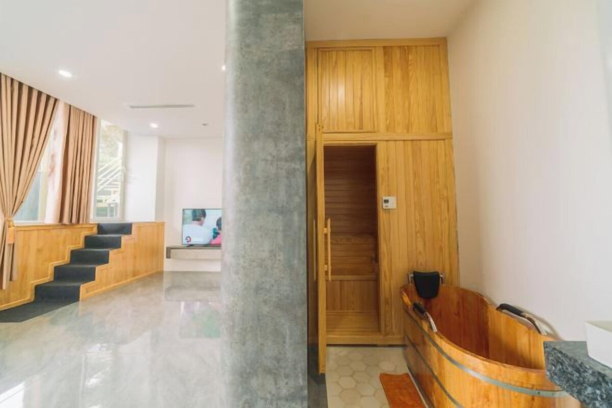 A modern hotel lobby with a wooden reception desk, a staircase, and a sauna area.