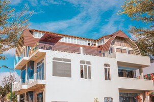 Un edificio de varios pisos con un balcón destacado, ventanas amplias y un cielo azul despejado.