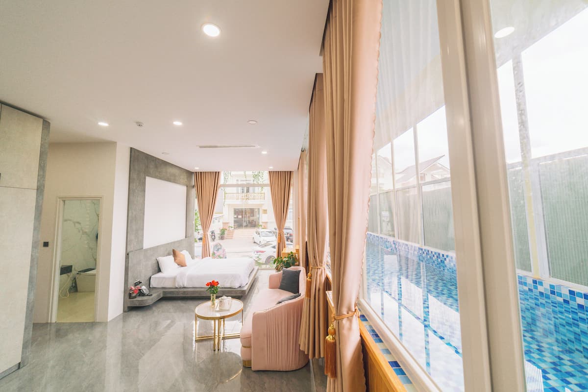 Habitación de hotel con cama, sofá, una mesita con un florero y vista a una piscina.