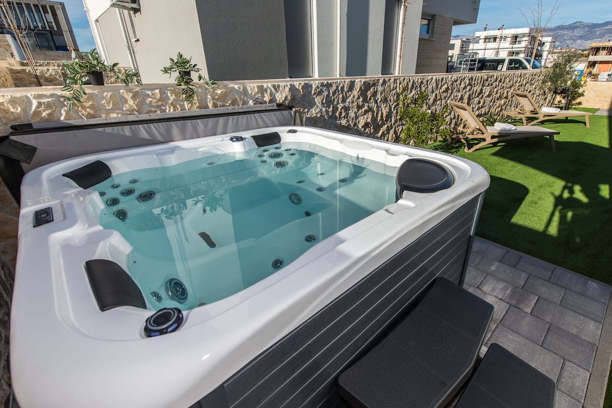 A hot tub with a stone wall backdrop, outdoor seating, and a view of buildings and mountains.
