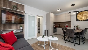 A modern living room with a sofa, two side tables, and a dining area with chairs and a table. - Apartments Mare B with pool  (Novalja)