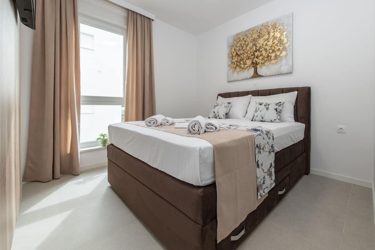 A bedroom with a bed, curtains, a window, and a wall-mounted artwork.