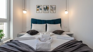 A neatly made bed with a blue headboard, white pillows, and a grey blanket. There are three wall-mounted light fixtures and three framed botanical prints above the bed. - Apartments Mare B with pool  (Novalja)
