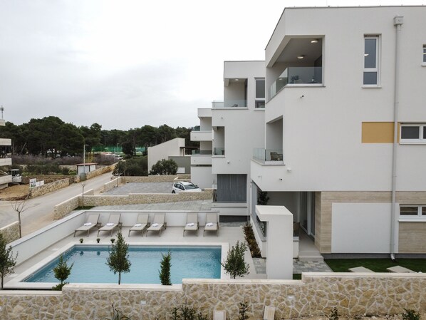 A modern building with a swimming pool, lounge chairs, and a stone wall.