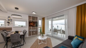 A modern living room with a sofa, dining table, and chairs. There is a balcony with a view of the city. - Apartments Mare B with pool  (Novalja)