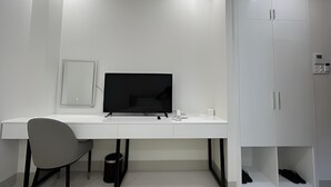 A modern, white room with a desk, chair, and a television. There is a cabinet with a shoe rack underneath. - Hala Hotel - by Bay Luxury (Ho Chi Minh City)