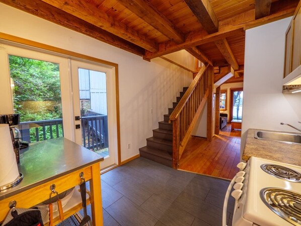 Une cuisine avec un escalier en bois, un coin repas offrant une vue sur l’extérieur et une grande fenêtre.