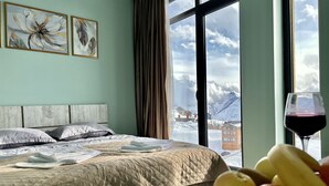 Une chambre d’hôtel avec un lit, une fenêtre donnant sur la montagne et une assiette de fruits.