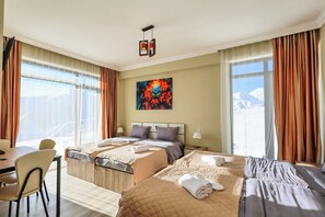 A hotel room with two beds, a dining area, and a large window with curtains. - Dandelion Hotel Gudauri (Kazbegi)