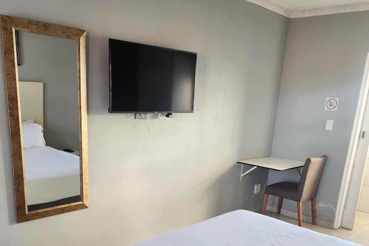 Ein Hotelzimmer mit Bett, Wandfernseher, Schreibtisch und Stuhl.
