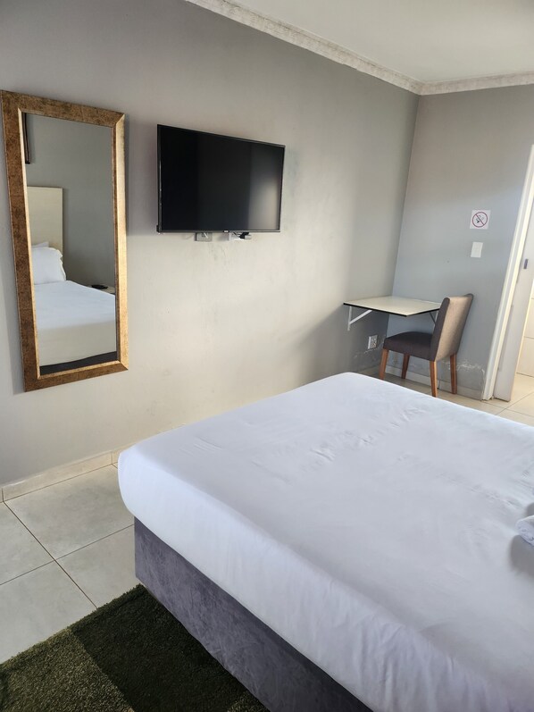 Una habitación de hotel con cama, televisión montada en la pared, escritorio y silla.