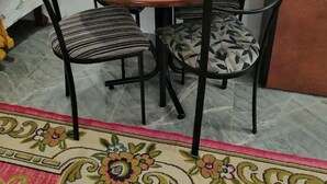 Un coin repas avec une table ronde et quatre chaises, une télécommande posée sur un set de table vert et un tapis à motifs.