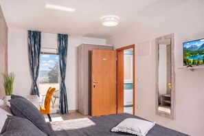 A modern bedroom with a bed, a TV, a balcony with a chair, and a view of the outdoors. - Family Resort Santa Maria II Room 201 (Novalja)