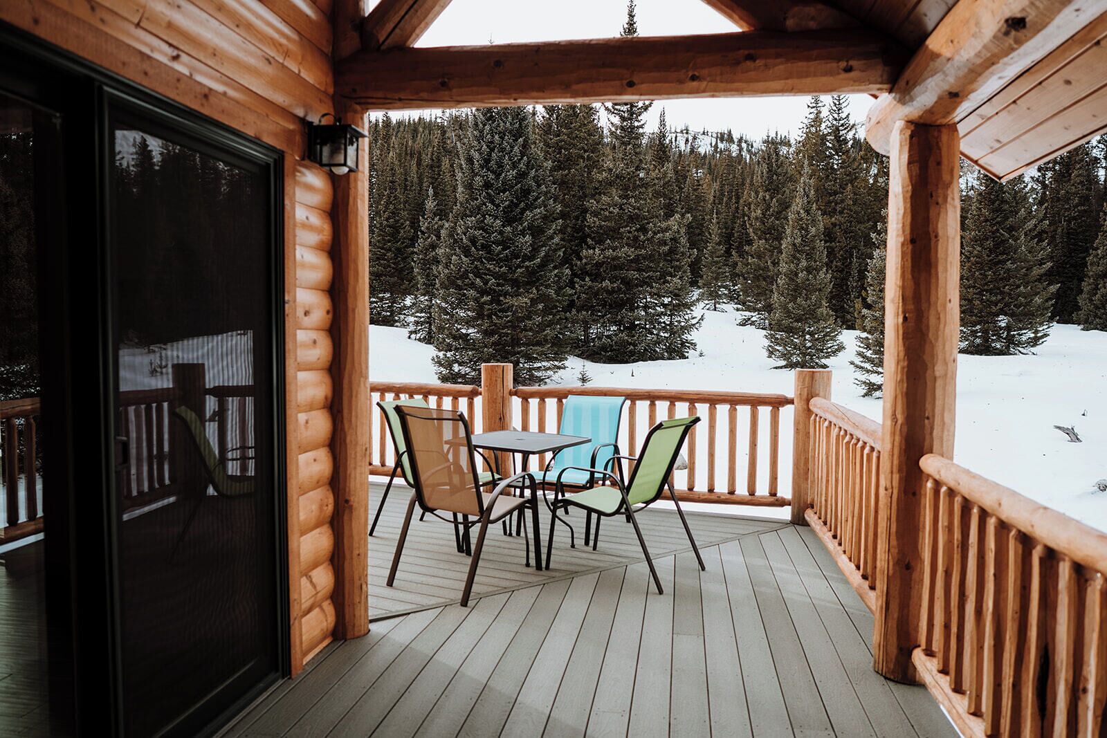 A wooden deck with a table and chairs, overlooking a snowy forest.