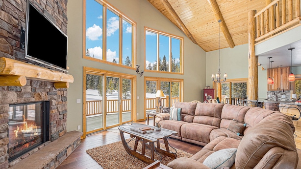 A spacious living room with a fireplace, large windows, a wooden ceiling, and a cozy seating area. - Log Cabin on 10 Acres with Loft and Soaker Tub. (Fairplay)