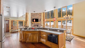 A spacious kitchen with wooden cabinets, a stone fireplace, and large windows offering a view of the outdoors. - Log Cabin on 10 Acres with Loft and Soaker Tub. (Fairplay)