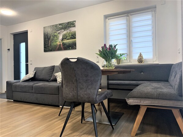 Uma sala de estar moderna com um sofá cinzento, uma poltrona cinzenta e uma mesa de centro de madeira com um vaso de flores.