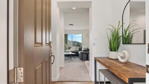 Un couloir mène à un espace de vie comprenant un canapé, une table basse et une plante posée sur une console en bois.