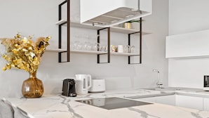 Une cuisine moderne dotée d’un plan de travail en marbre, d’une cuisinière encastrée, d’une machine à café et d’un vase contenant des fleurs séchées.