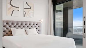 Une chambre moderne avec une tête de lit capitonnée, du linge de lit blanc et des œuvres d’art abstraites accrochées au mur.